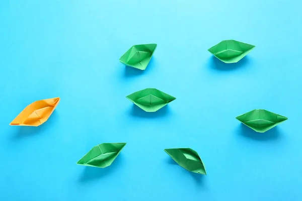 Orange origami båt bland gröna på färg bakgrund. Begreppet unikt — Stockfoto