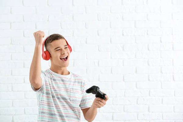 Happy teenager boy with game pad on white brick background — Stock Photo, Image