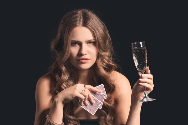 Beautiful young woman with playing cards and glass of champagne on dark background — Zdjęcie stockowe