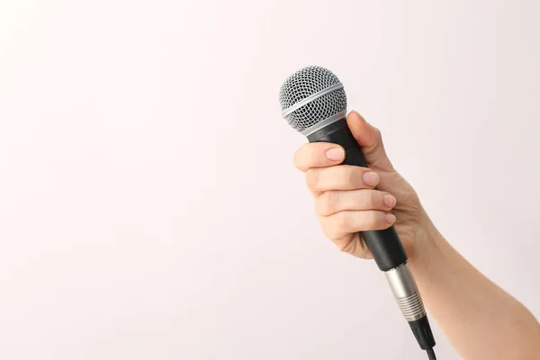 Mano femminile con microfono su sfondo chiaro — Foto Stock