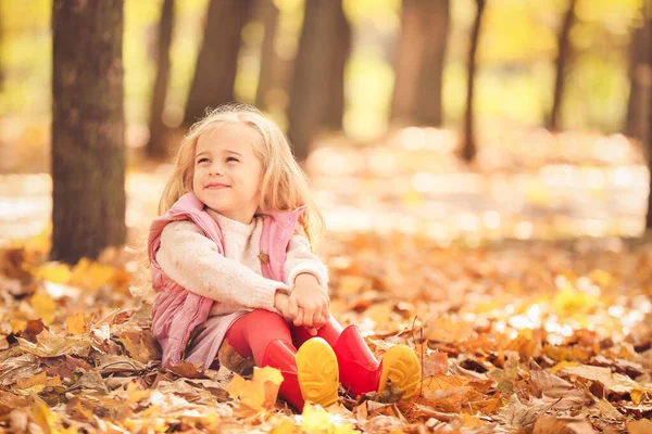 Cute little girl sitting in autumn park — Stock Photo, Image