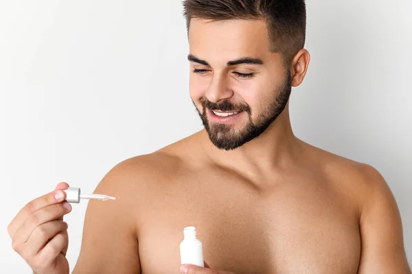 Joven guapo con producto cosmético sobre fondo claro — Foto de Stock