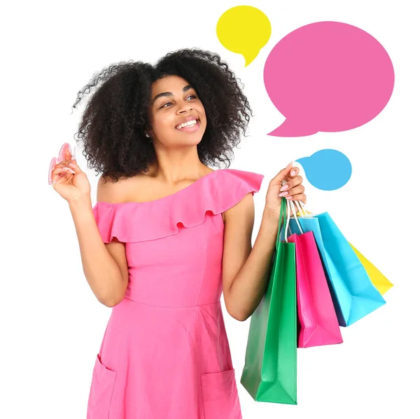 Beautiful African-American woman with shopping bags and blank speech bubbles on white background — ストック写真
