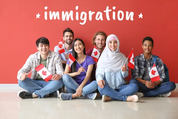 Mot IMMIGRATION et groupe d'étudiants avec des drapeaux canadiens assis près du mur de couleur — Photo