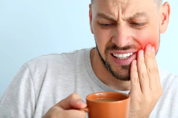 Man med känsliga tänder och kopp hett kaffe på färg bakgrund — Stockfoto