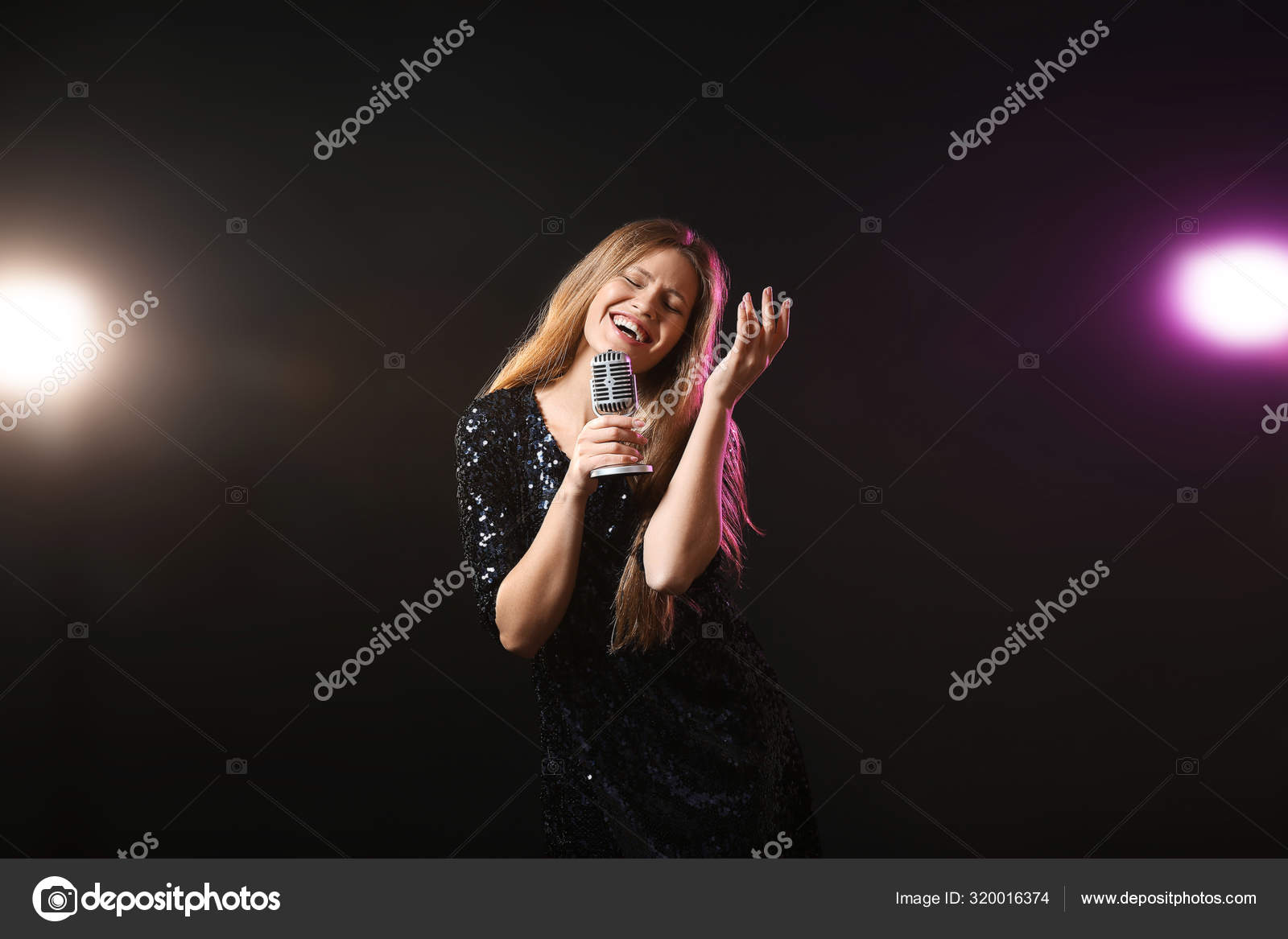 Beautiful young female singer with microphone on stage Stock Photo by