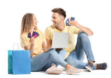 Kredi kartları, alışveriş çantaları ve beyaz arka planda dizüstü bilgisayarı olan genç bir çift.