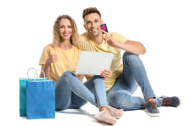 Kredi kartı, alışveriş torbaları ve beyaz arka planda dizüstü bilgisayarı olan genç bir kadın.