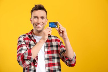 Young man with credit card on color background