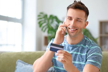 Kredi kartlı genç adam cep telefonuyla konuşuyor.