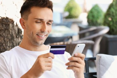 Kafede oturan kredi kartı ve cep telefonu olan genç bir adam.