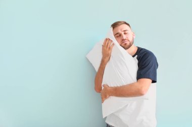 Hafif arka planda yastığı olan uykulu genç bir adam.