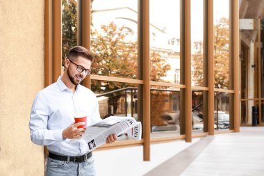 Dışarıda gazete ve kahve taşıyan yakışıklı bir adam.