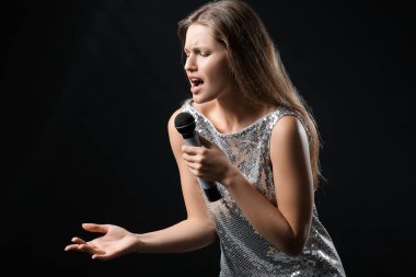 Koyu arkaplanda mikrofonu olan güzel bir bayan şarkıcı.