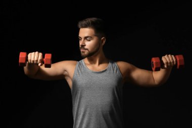 Koyu arka plan üzerinde dumbbells ile sportif genç adam