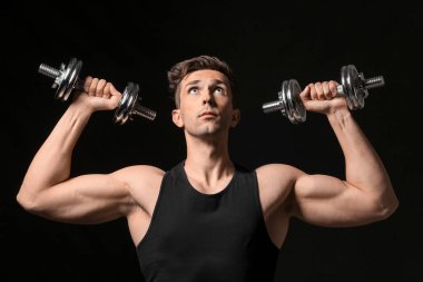 Koyu arka plan üzerinde dumbbells ile sportif genç adam