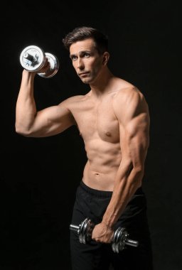 Koyu arka plan üzerinde dumbbells ile sportif genç adam