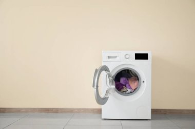 Modern washing machine with laundry near color wall clipart