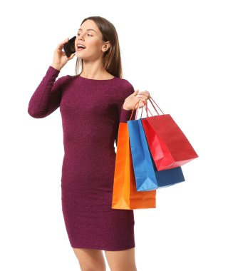 Alışveriş torbalarıyla beyaz arka planda telefonla konuşan güzel genç bir kadın.