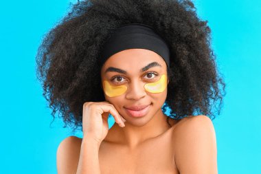 Portrait of beautiful African-American woman with under-eye patches on color background clipart