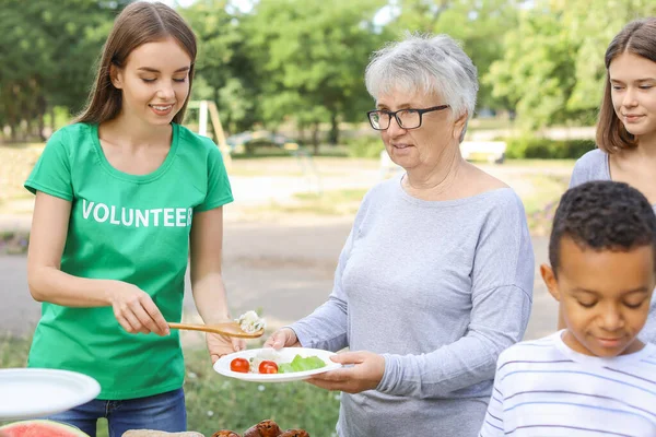 Young volunteer giving food to poor people outdoors