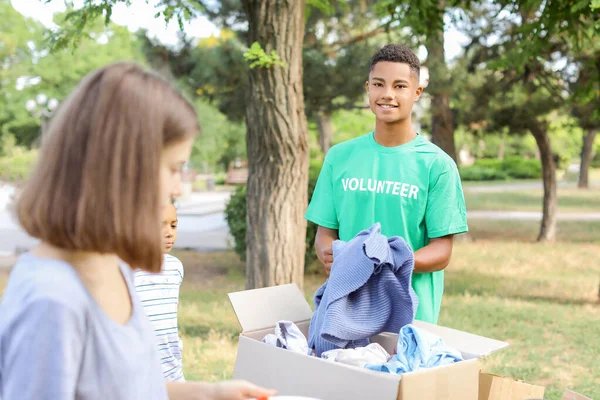 Joven voluntario afroamericano dando ropa nueva para los pobres al aire libre — Foto de Stock