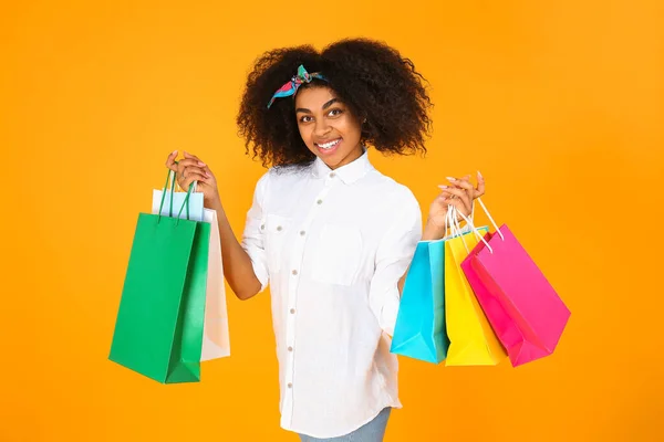 Krásná afroamerická žena s nákupními taškami na barevném pozadí — Stock fotografie