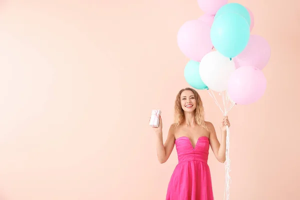 Красивая молодая женщина с воздушными шарами и подарок на цветном фоне — стоковое фото