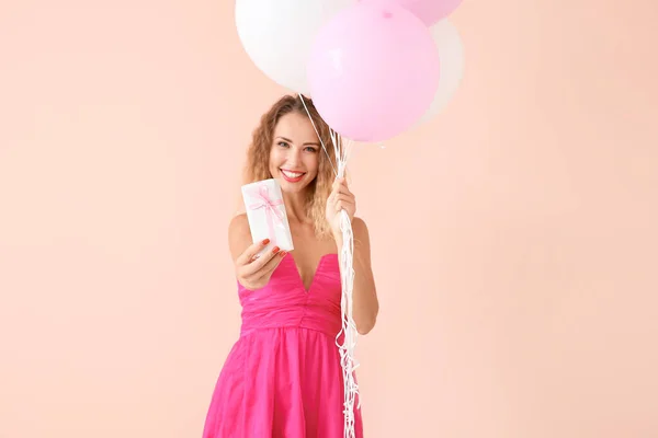 Hermosa mujer joven con globos y regalo en el fondo de color —  Fotos de Stock