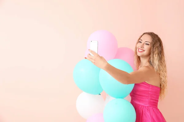 Belle jeune femme avec des ballons prenant selfie sur fond de couleur — Photo