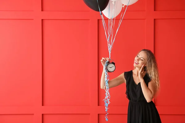Mooie jonge vrouw met ballonnen en klok op kleur achtergrond — Stockfoto