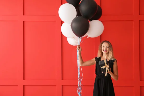 Hermosa mujer joven con globos y regalo en el fondo de color —  Fotos de Stock