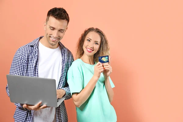 Young couple with credit card and laptop on color background — Stock Photo, Image