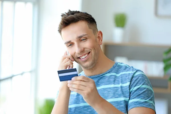 Mladý muž s kreditní kartou mluví mobilním telefonem doma — Stock fotografie