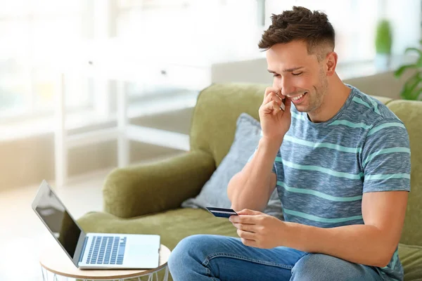 Young man with credit card talking by mobile phone at home — Stock Photo, Image