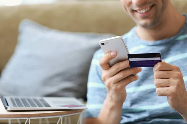 Young man with credit card and mobile phone at home, closeup — Stock Photo, Image