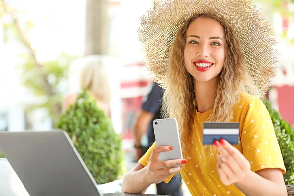 Jeune femme avec carte de crédit, téléphone portable et ordinateur portable assis dans un café — Photo