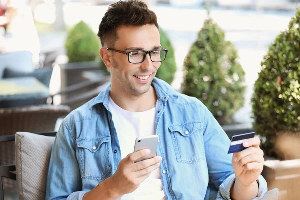 Jeune homme avec carte de crédit et téléphone portable dans le café — Photo