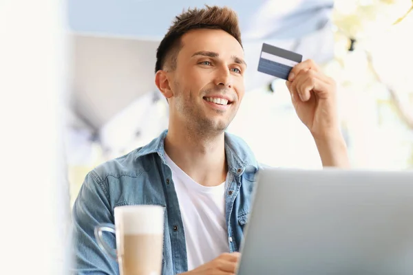 Young man with credit card and laptop sitting in cafe — Stock Photo, Image