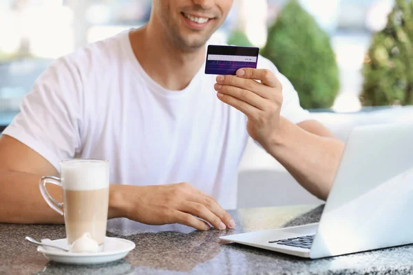 Jeune homme avec carte de crédit et ordinateur portable assis dans un café — Photo