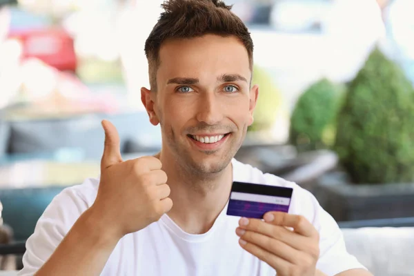 Mladý muž s kreditní kartou ukazující pohyb palcem nahoru venku — Stock fotografie
