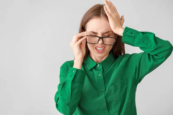 Junge Frau leidet an Kopfschmerzen auf leichtem Hintergrund — Stockfoto