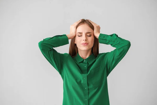 Junge Frau leidet an Kopfschmerzen auf leichtem Hintergrund — Stockfoto