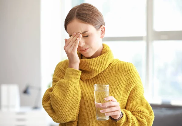 Молода жінка зі склянкою води, що страждає від головного болю вдома — стокове фото