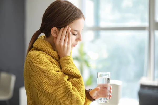 Jeune femme avec un verre d'eau souffrant de maux de tête à la maison — Photo