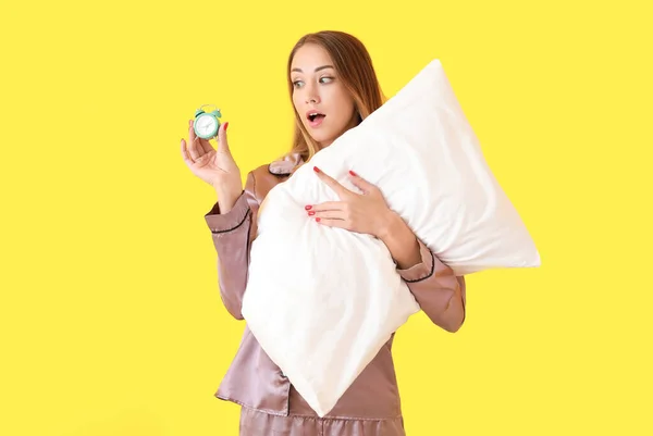 Surprised young woman with pillow and alarm clock on color background — Stock Photo, Image