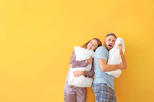 Sleepy young couple with pillows on color background — Stock Photo, Image