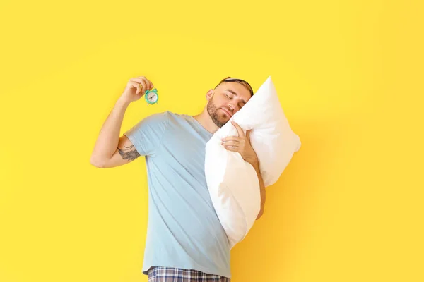 Joven con almohada y reloj despertador sobre fondo de color — Foto de Stock