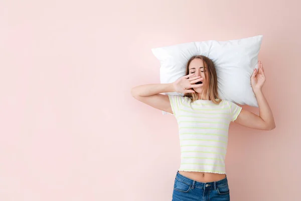 Сонная молодая женщина с подушкой на цветном фоне — стоковое фото