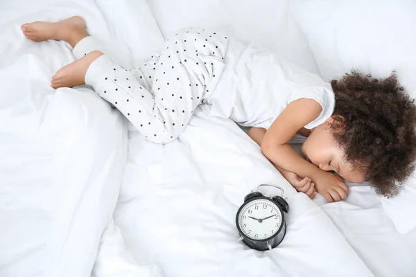 Little African-American girl with alarm clock sleeping in bed — Stock Photo, Image